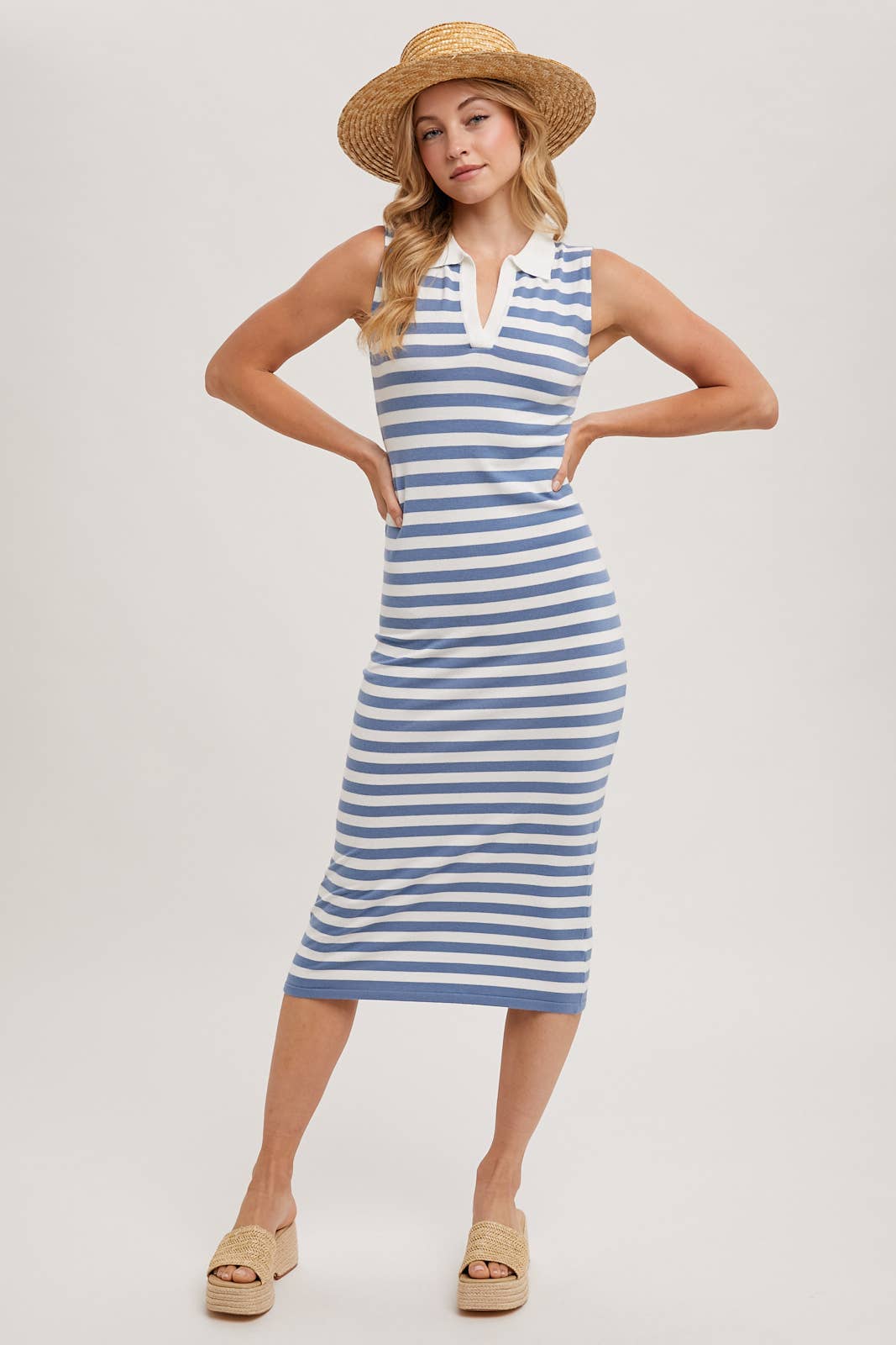Woman wearing a blue and white striped dress with a straw hat on a plain background